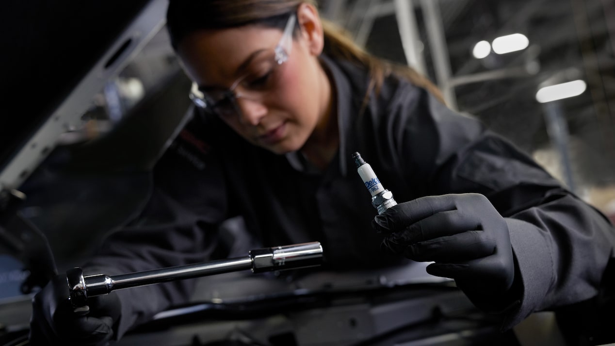 GM Technician Holding a Spark Plug and Working on a Vehicle