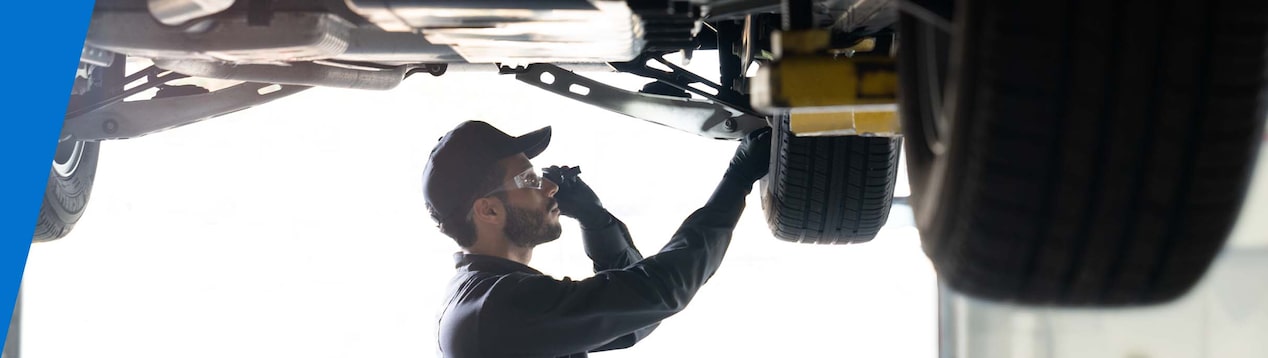 GM Technician Standing Under a Vehicle on a Lift Inspecting the Wheel