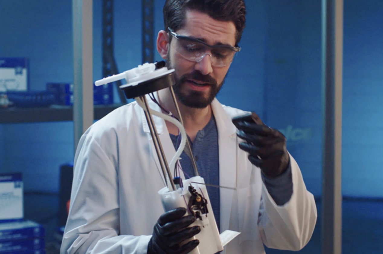 A Man Wearing a Lab Coat and Goggles Tests an Automotive Part